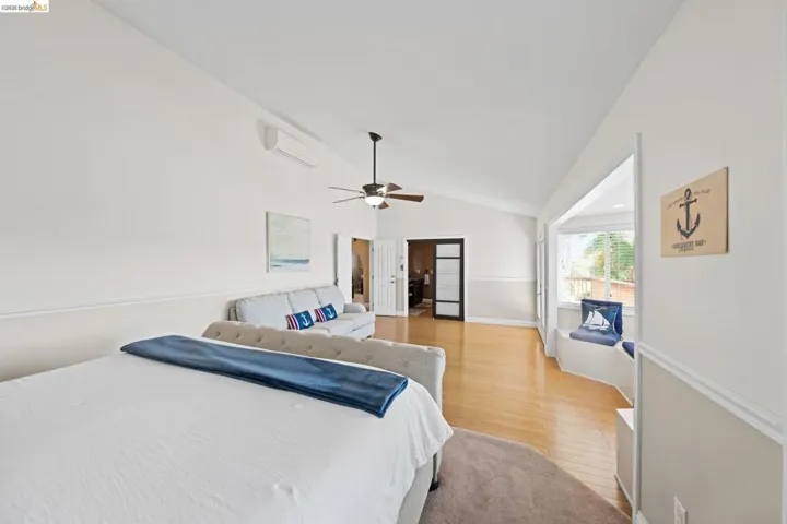 Bedroom featuring lofted ceiling, light wood finished floors, a wall mounted air conditioner, and a ceiling fan