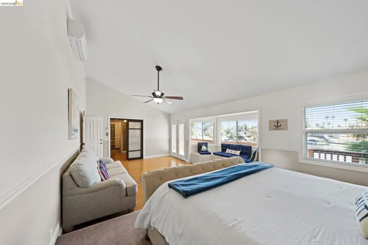 Bedroom with a wall unit AC, a ceiling fan, access to exterior, light wood-style floors, and high vaulted ceiling