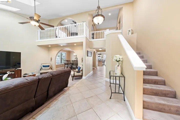 Tiled living room with a towering ceiling, arched walkways, stairs, ceiling fan, and recessed lighting
