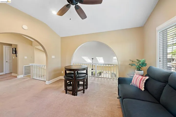 Living room featuring light colored carpet, vaulted ceiling, a ceiling fan, and arched walkways