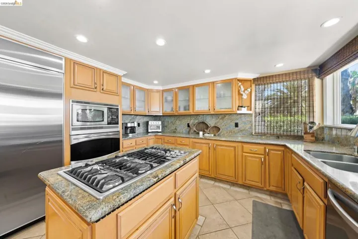Kitchen featuring light stone counters, a kitchen island, built in appliances, light tile patterned flooring, and backsplash