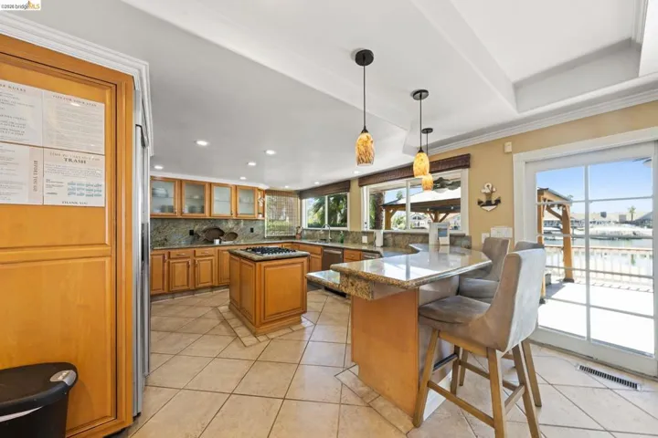 Kitchen featuring glass insert cabinets, hanging light fixtures, decorative backsplash, light stone counters, and a kitchen breakfast bar