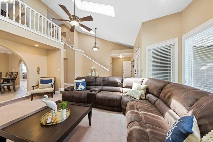 Living room featuring arched walkways, a skylight, ceiling fan, high vaulted ceiling, and stairway
