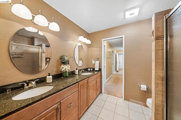 Bathroom with a textured wall, light tile patterned flooring, a stall shower, and double vanity