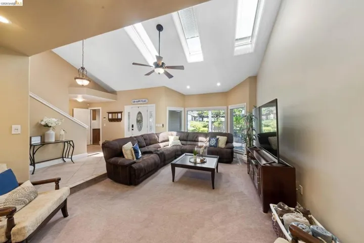 Living area featuring high vaulted ceiling, light carpet, ceiling fan, a skylight, and light tile patterned floors