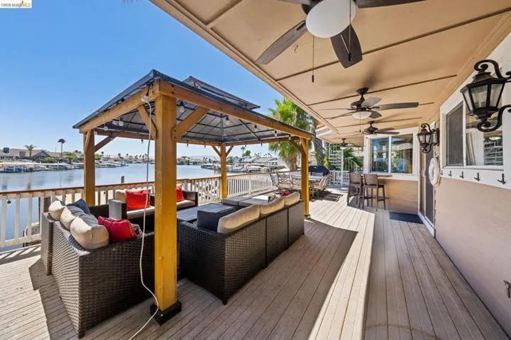 Wooden terrace with an outdoor living space, a water view, a gazebo, and a ceiling fan