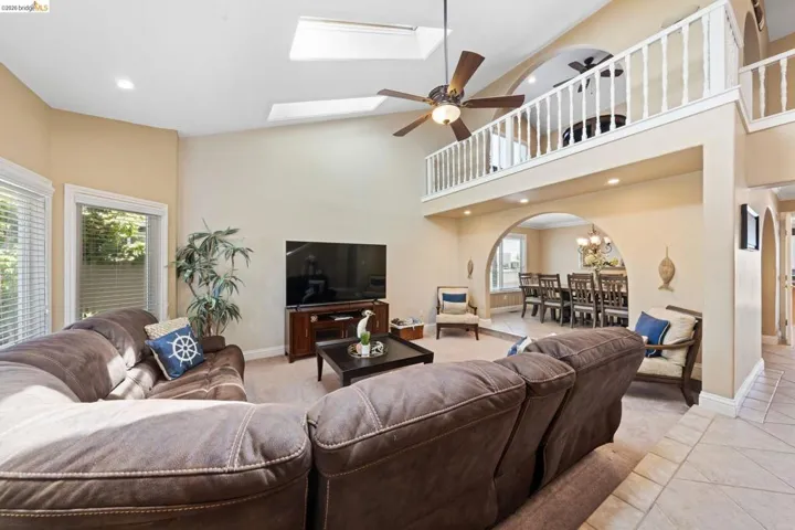 Living area featuring a ceiling fan, recessed lighting, light tile patterned floors, arched walkways, and a towering ceiling
