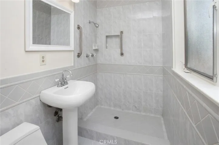 Primary en suite bathroom with custom tiled step-in shower, pedestal sink, and privacy window.