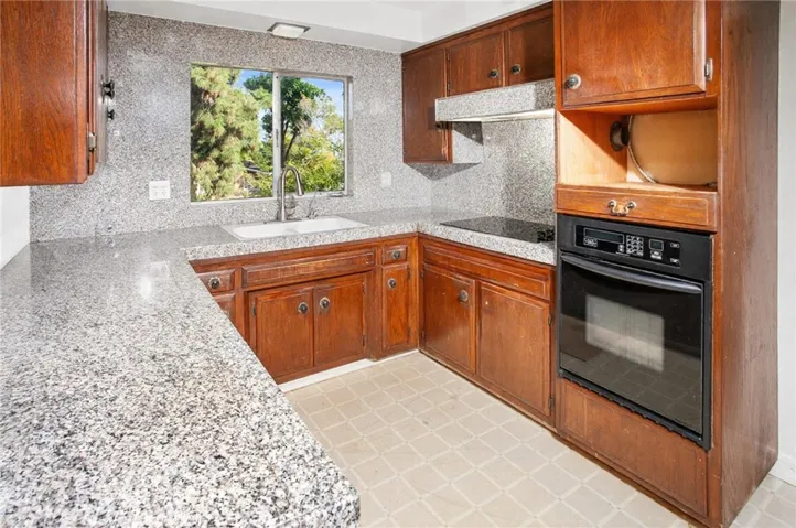 The kitchen features ceiling height wood grain cabinetry, granite countertops, full tile backsplash, electric cooktop, built-in oven, dishwasher, dual basin sink, and a bright window with neighborhood views.
