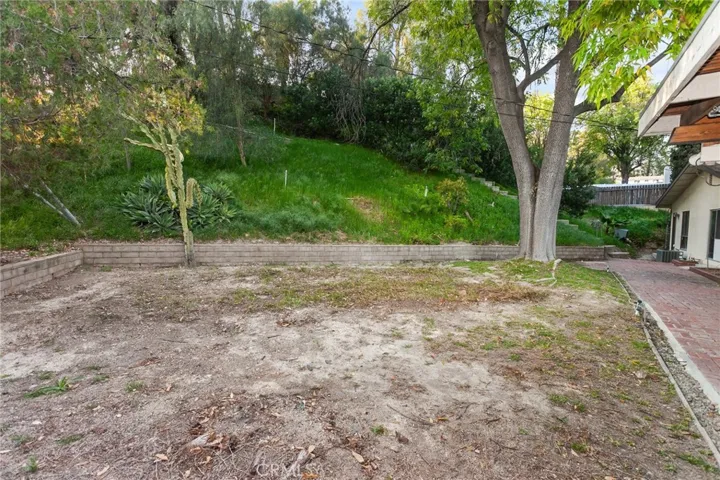 The private side and backyard offers a peaceful park-like setting with lush natural landscaping, mature shade trees, and an oversized covered brick patio with lighting, raised brick planters, and manicured hedges, creating an inviting outdoor setting for relaxing or entertaining.