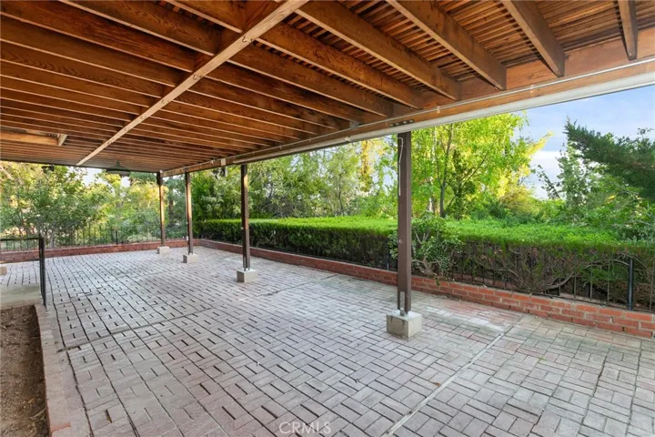 The private side and backyard offers a peaceful park-like setting with lush natural landscaping, mature shade trees, and an oversized covered brick patio with lighting, raised brick planters, and manicured hedges, creating an inviting outdoor setting for relaxing or entertaining.