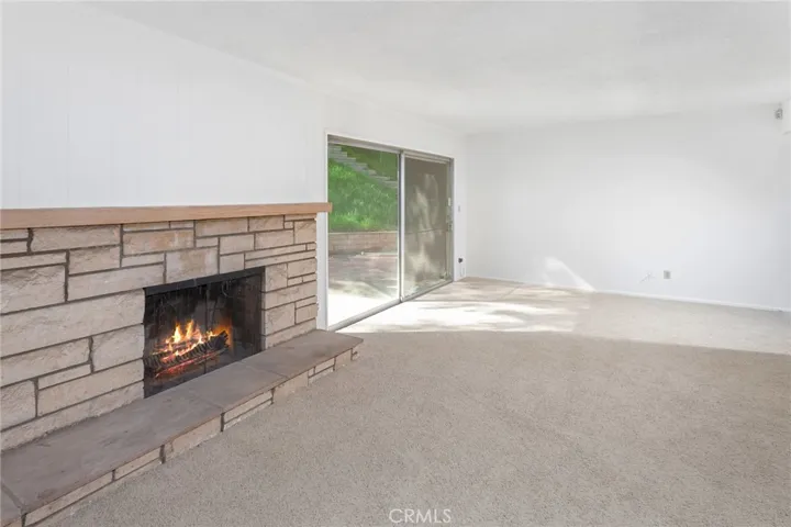 Double wood entry doors open to a freshly painted open concept floor plan featuring a spacious living room with new carpet, raised hearth stone fireplace, and sliding glass doors that lead to the backyard.