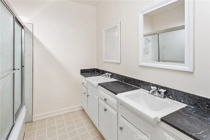 The guest bathroom offers a granite countertop vanity with dual basins, new mirrors, and a glass enclosed tub and shower combination.