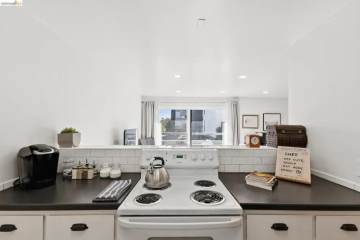 Kitchen with dark countertops, white electric range oven, white cabinets, and backsplash