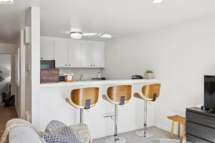 Kitchen featuring tile countertops, a breakfast bar area, white cabinetry, decorative backsplash, and a peninsula