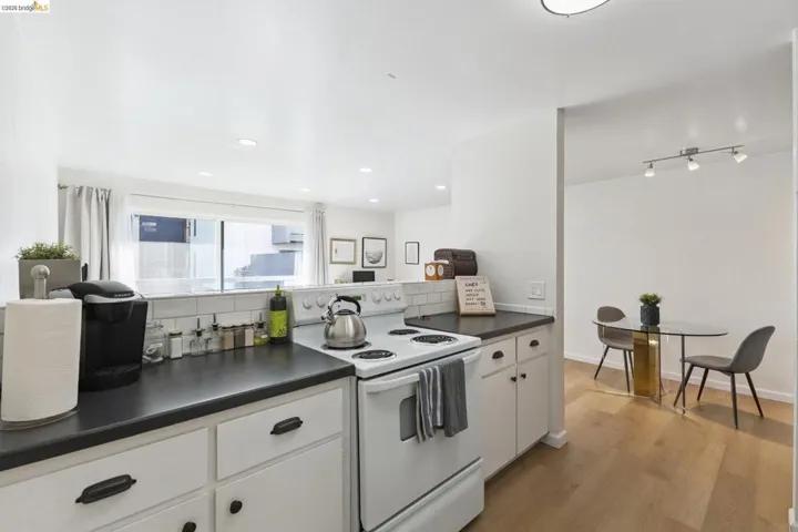 Kitchen with white electric stove, dark countertops, white cabinets, light wood-type flooring, and recessed lighting