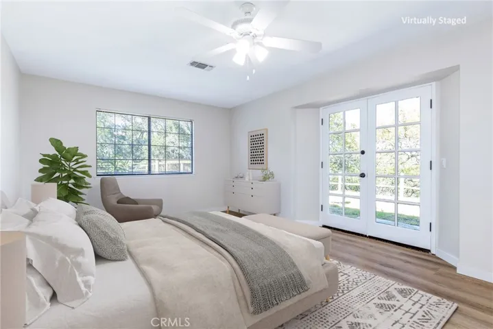 The primary suite is located on the main floor and has vinyl plank flooring and a French door. Photo has been virtually staged.