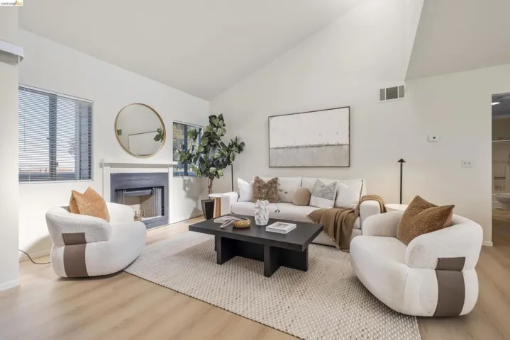 Living room with a glass covered fireplace, light wood-style floors, and lofted ceiling