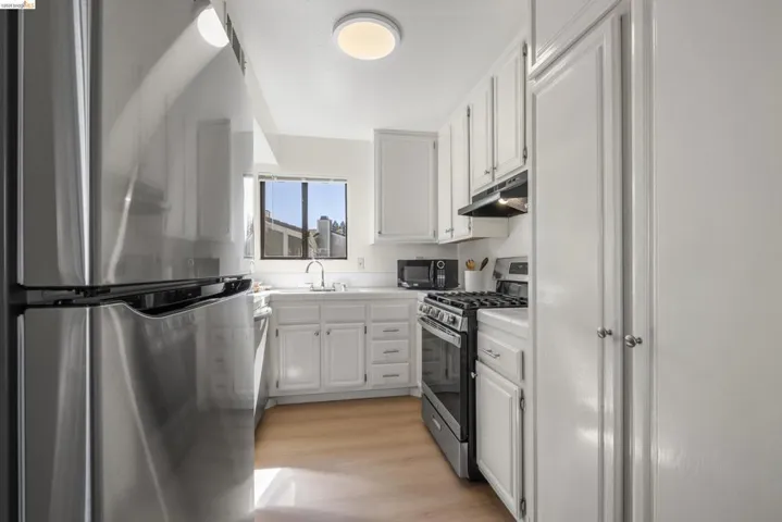 Kitchen with stainless steel appliances, white cabinets, light countertops, and light wood-style floors