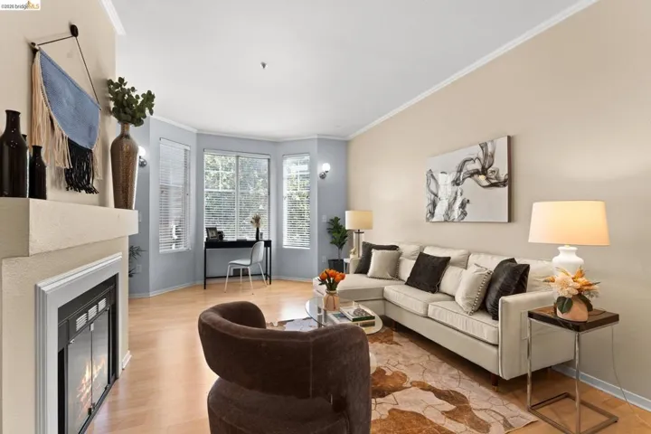 Living room featuring a glass covered fireplace, crown molding, light wood-style flooring, and an office area