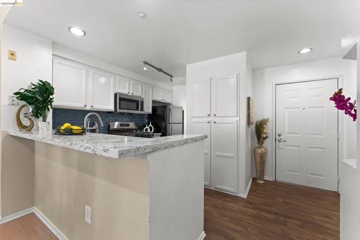 Kitchen with white cabinetry, a peninsula, light stone counters, stainless steel appliances, and dark wood-type flooring
