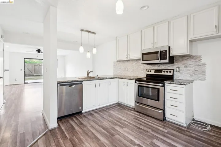 Kitchen with stainless steel appliances, white cabinetry, decorative backsplash, and a ceiling fan