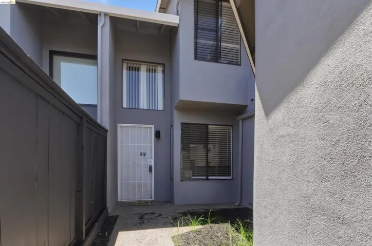 Modern stucco exterior with multiple windows, a security screen door, and exterior lighting fixtures