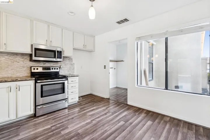 Kitchen with stainless steel appliances, white cabinetry, backsplash, dark stone counters, and dark wood-type flooring