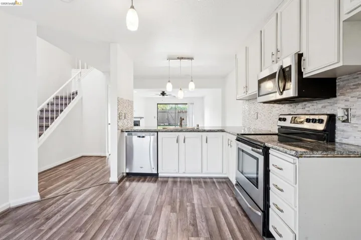 Kitchen with stainless steel appliances, white cabinetry, dark stone countertops, tasteful backsplash, and dark wood-style flooring