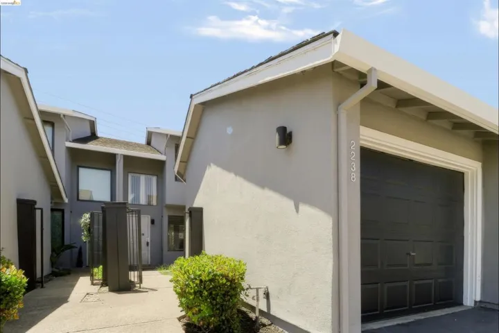 Contemporary stucco exterior featuring a black panel garage door, recessed outdoor lighting, and modern house numbers