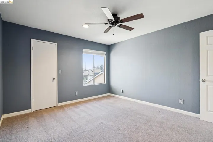 Empty room with ceiling fan and light carpet