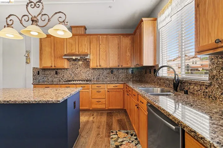 Kitchen featuring light wood-type flooring, dishwasher, light stone countertops, decorative backsplash, and decorative light fixtures