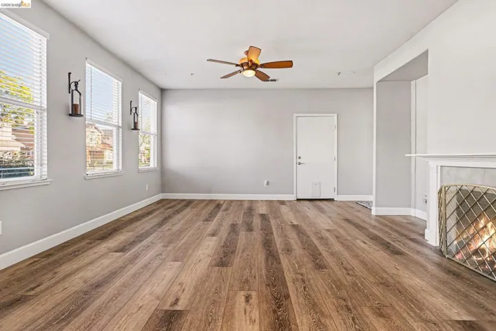 Unfurnished living room featuring wood finished floors, a ceiling fan, and a tiled fireplace
