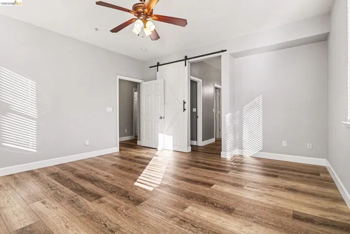 Unfurnished bedroom featuring a barn door, dark wood-type flooring, and a ceiling fan