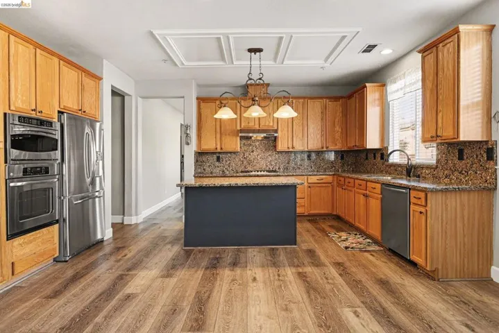 Kitchen featuring dark stone countertops, a kitchen island, stainless steel appliances, dark wood finished floors, and hanging light fixtures