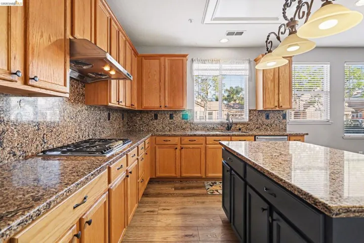 Kitchen featuring two tone color scheme, dark stone counters, light wood finished floors, stainless steel gas cooktop, and tasteful backsplash