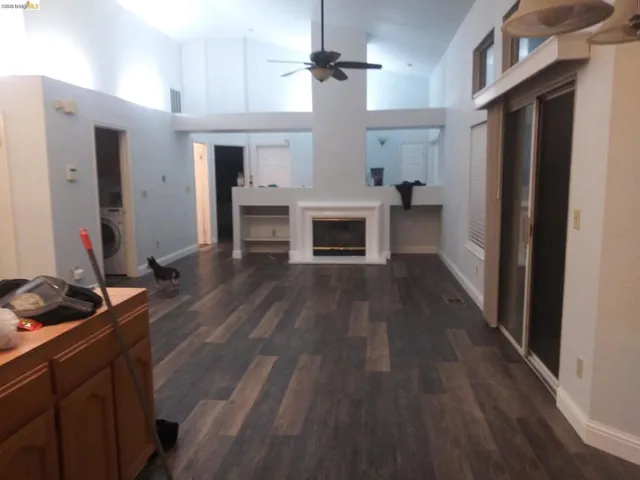 Living room with vaulted ceiling, a ceiling fan, washer / clothes dryer, a glass covered fireplace, and dark wood-style flooring