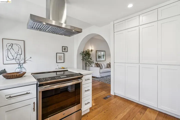 Kitchen featuring stainless steel electric range oven, island exhaust hood, white cabinets, light wood finished floors, and light stone counters