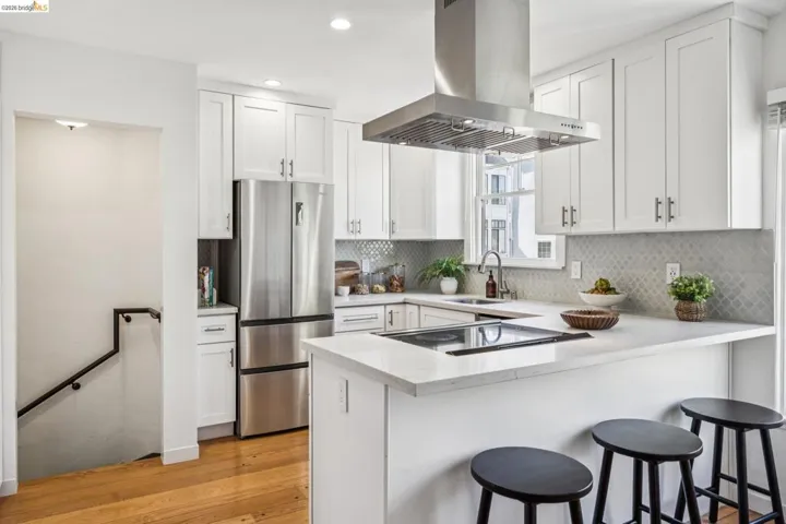 Kitchen with island exhaust hood, a breakfast bar area, white cabinets, freestanding refrigerator, and recessed lighting