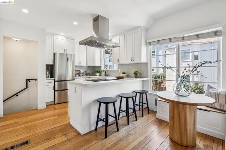 Kitchen with island range hood, white cabinetry, freestanding refrigerator, a breakfast bar, and light wood finished floors