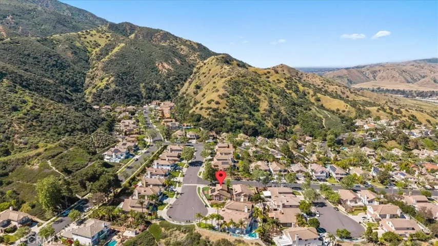 Expansive aerial view capturing the surrounding community, nearby hills, and scenic landscape, providing context for the home’s location.