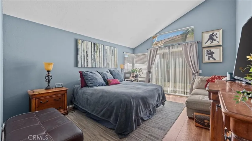 A comfortable primary suite with vaulted ceilings, soft natural light, and direct access to the backyard through sliding glass doors, creating a peaceful retreat.