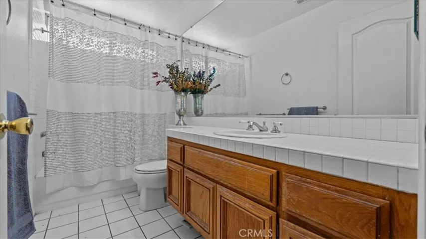This secondary bathroom includes a large vanity, tiled flooring, and a shower-tub combination, designed for everyday convenience.