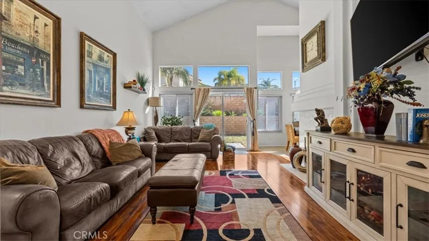 This inviting living room showcases vaulted ceilings, rich wood flooring, and abundant natural light from large windows and sliding glass doors. A cozy fireplace and open layout make it ideal for everyday living and entertaining.
