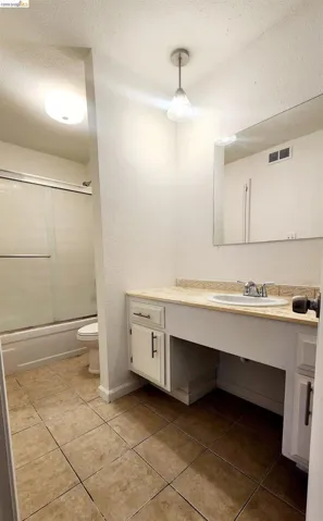 Full bathroom with a textured wall, a textured ceiling, vanity, light tile patterned floors, and enclosed tub / shower combo