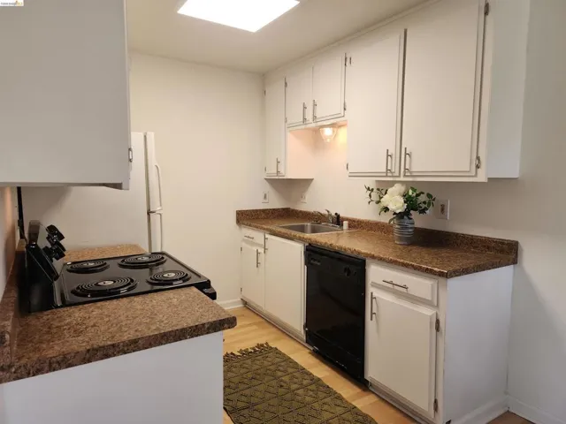 Kitchen featuring dark countertops, black appliances, light wood-style flooring, and white cabinets