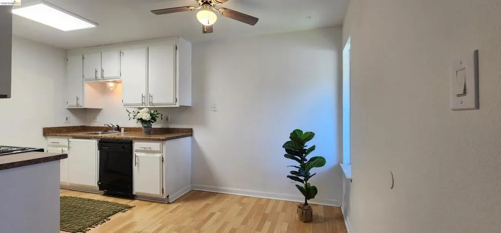 Kitchen featuring light wood-style flooring, white cabinets, black dishwasher, dark countertops, and a ceiling fan