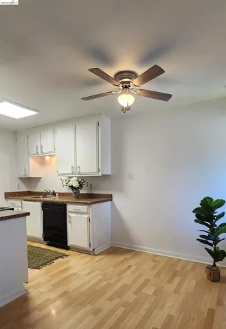 Kitchen with white cabinetry, light wood-type flooring, black dishwasher, and ceiling fan