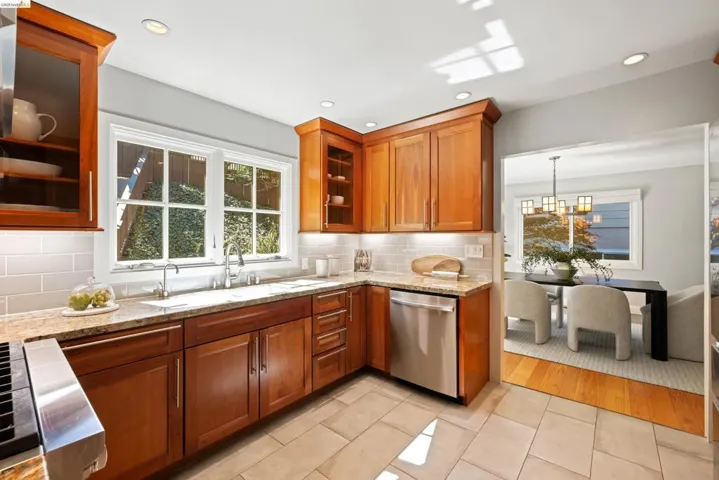 Kitchen featuring light tile patterned flooring, light stone countertops, wood finish cabinetry, glass insert cabinets, and dishwasher