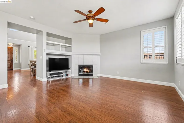Unfurnished living room with built in features, dark wood-style floors, a fireplace, and a ceiling fan